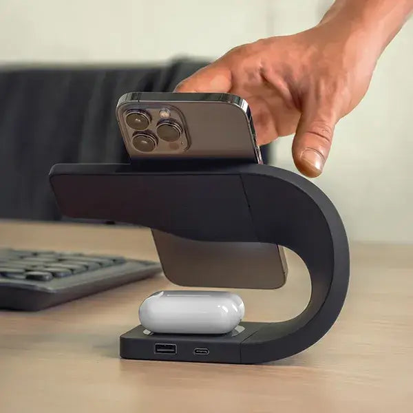 Hand placing iPhone on black Simpli MagSafe charging stand charging Apple devices like iPhone and AirPods on desk