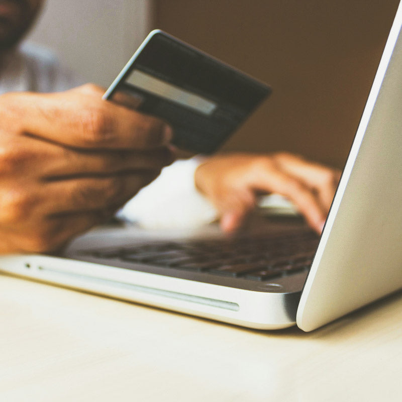 Close-up view of a man using a credit card and laptop to make an online purchase, showcasing secure e-commerce transaction with a focus on keyboard and credit card details.