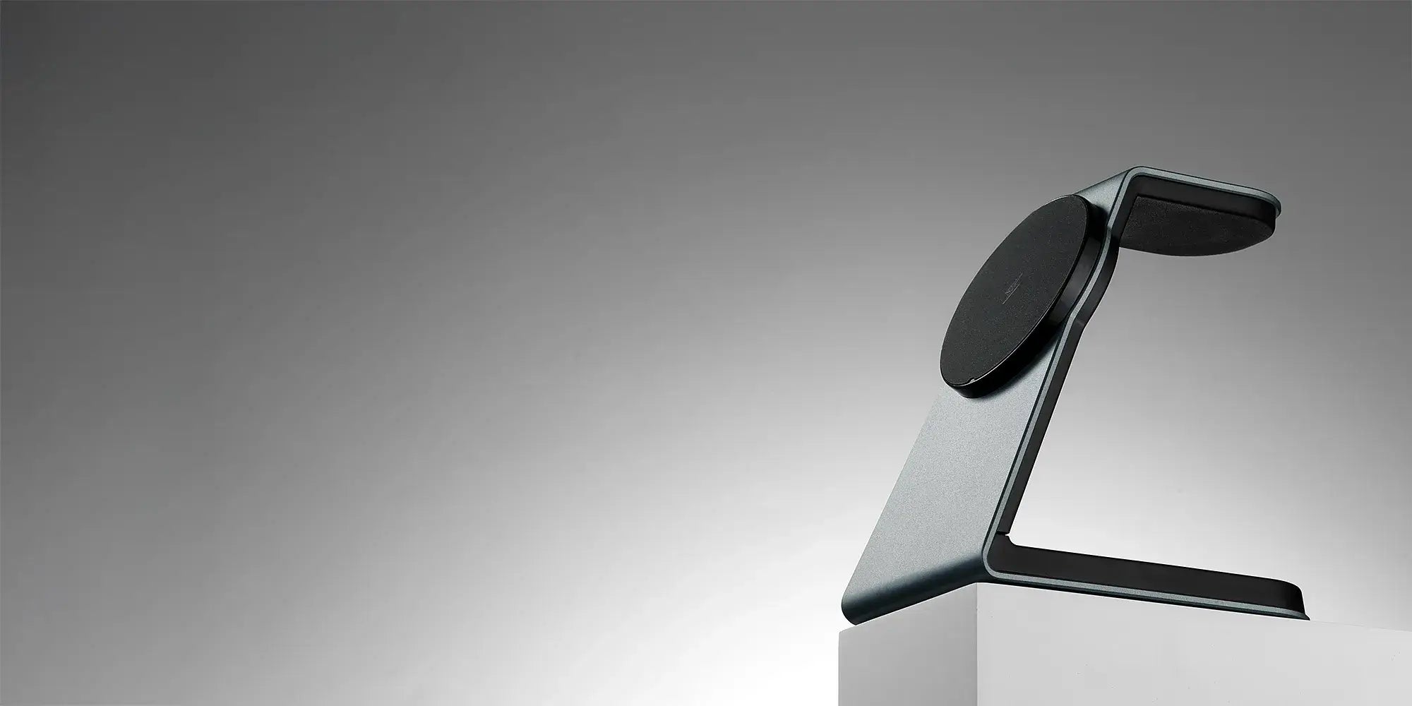 Slate gray Magnitis MagSafe charging stand on white pedestal against gradient backdrop