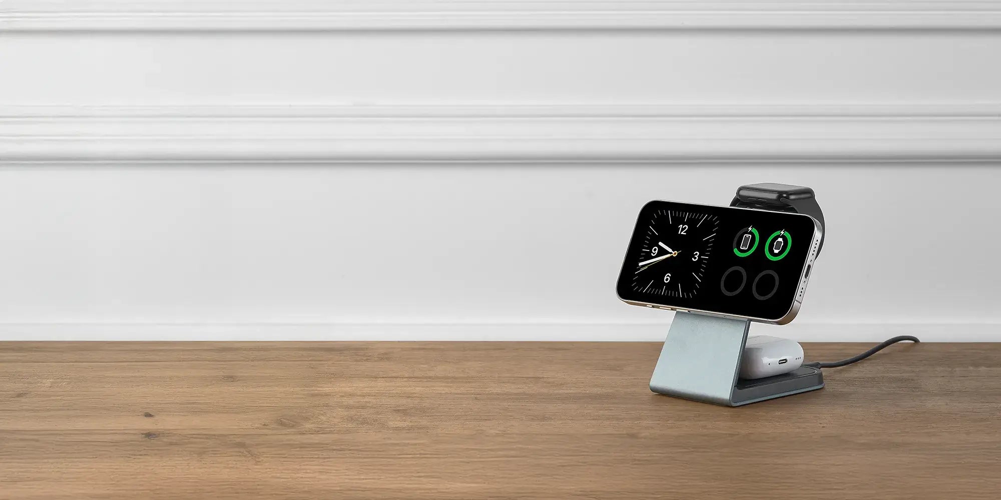 Slate gray Magnitis MagSafe charging stand in standby mode holding iPhone showing clock and battery icons on wooden desk