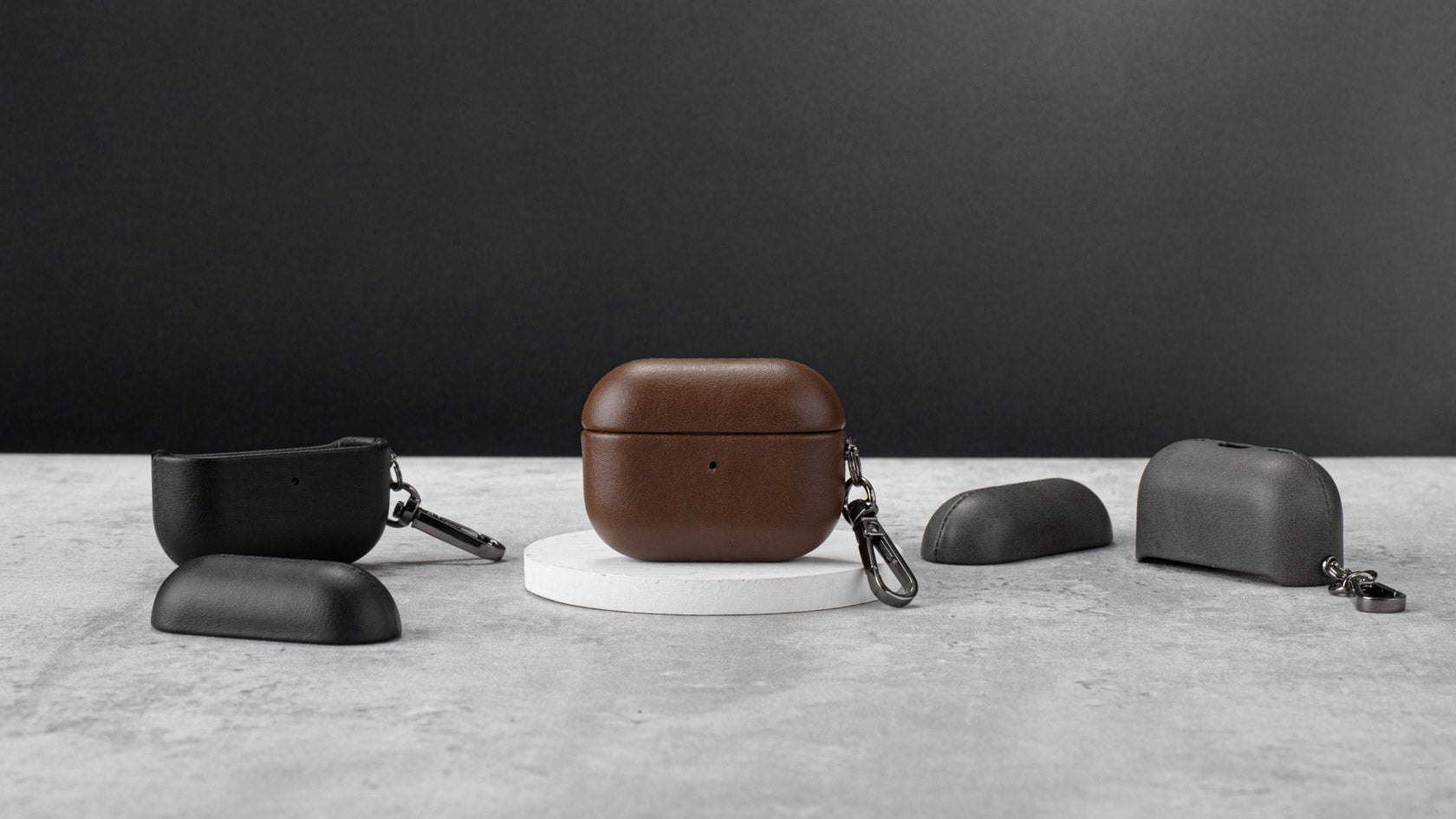 AirPods Pro Leather Cover, AURA, Midnight, Espresso & Graphite Colors, sitting on a product stand. 